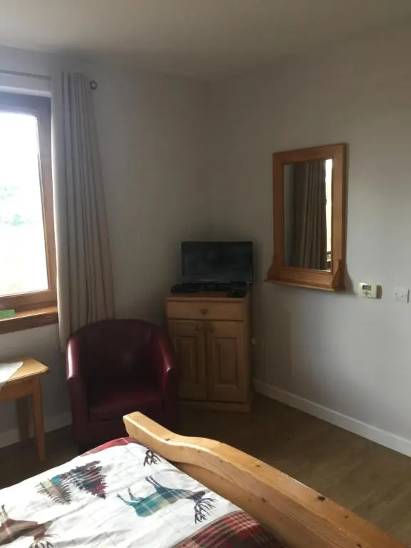 a bedroom with a bed and a chair and a mirror at Doura Lodge in Inverness