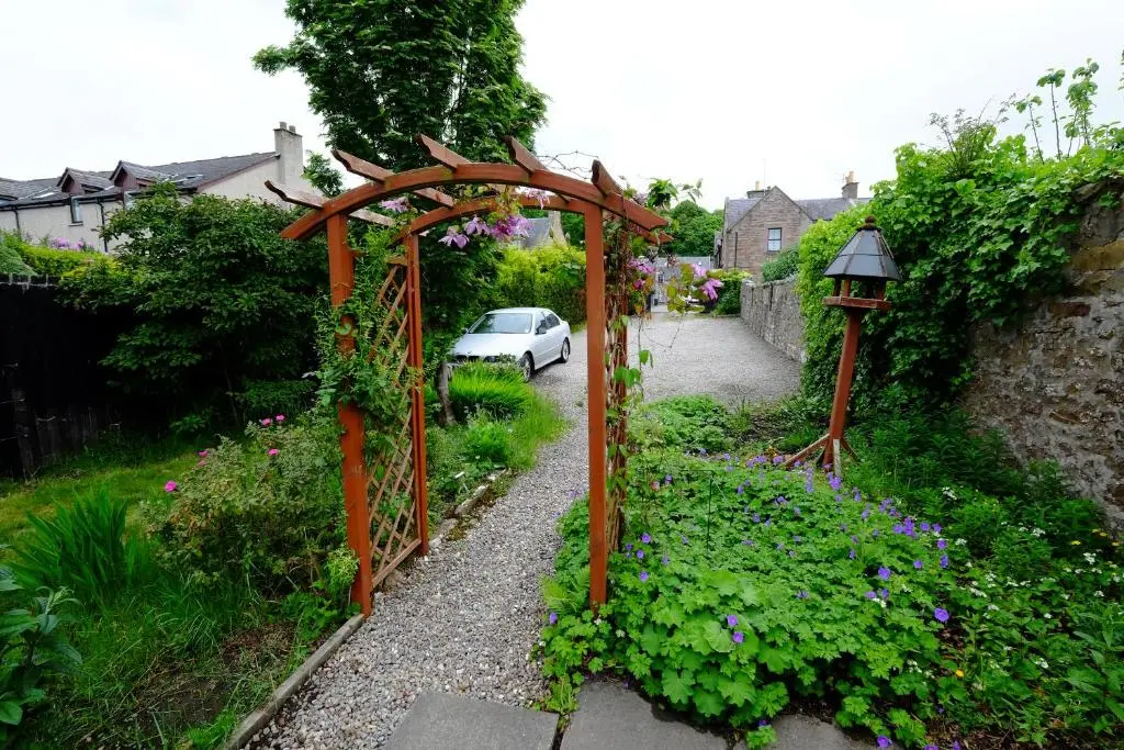 a garden with an arbor and a car on a driveway at Talisker Guest House in Inverness