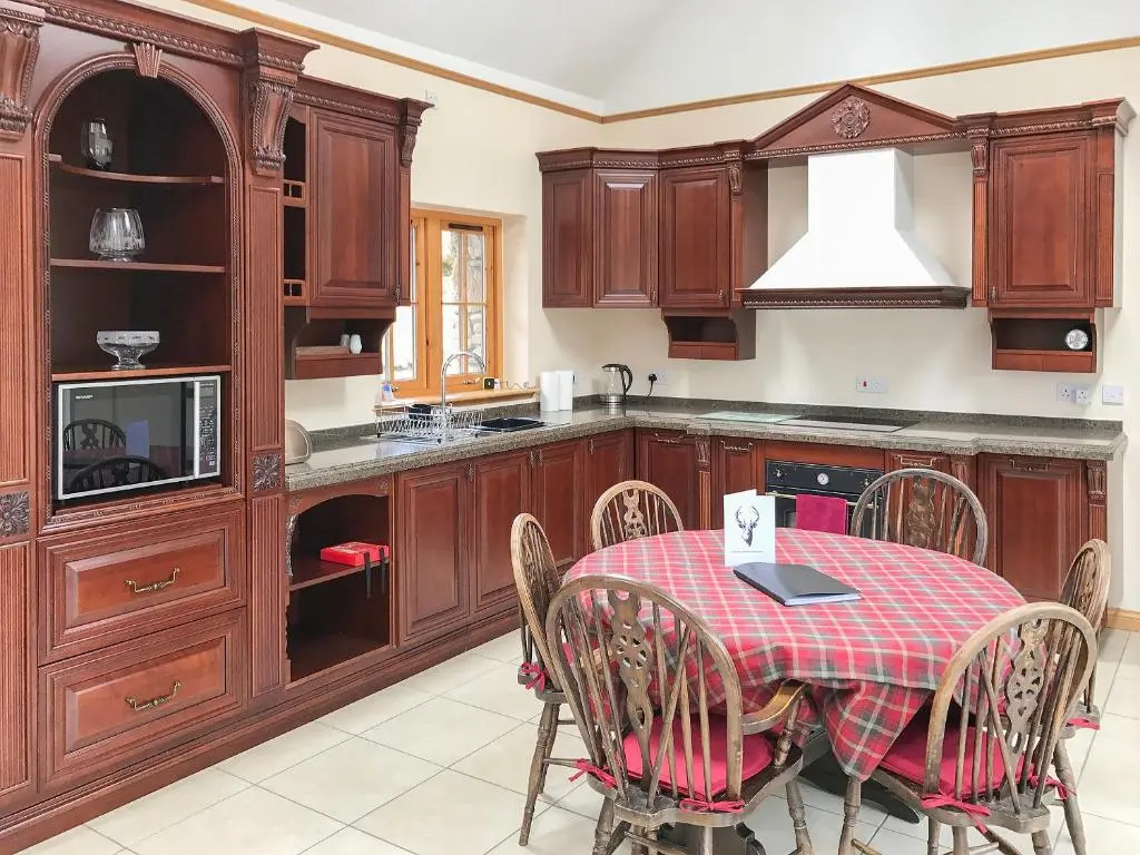 a kitchen with wooden cabinets and a table with chairs at Turin Nurin Cottage in Tomatin