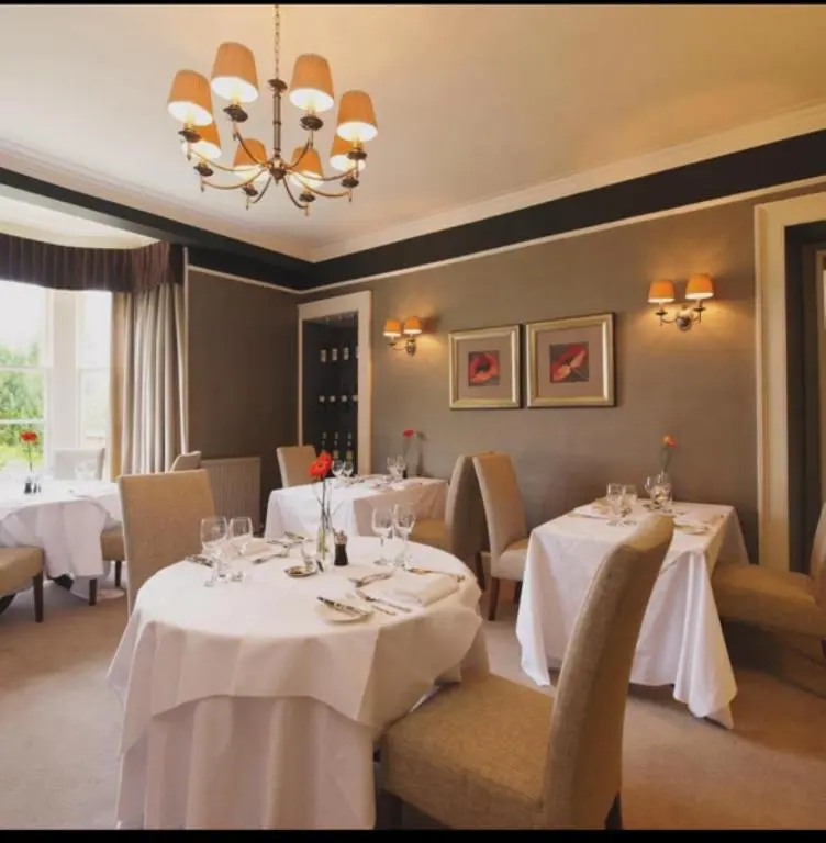 a restaurant with white tables and chairs and a chandelier at Loch Ness Country House Hotel in Inverness