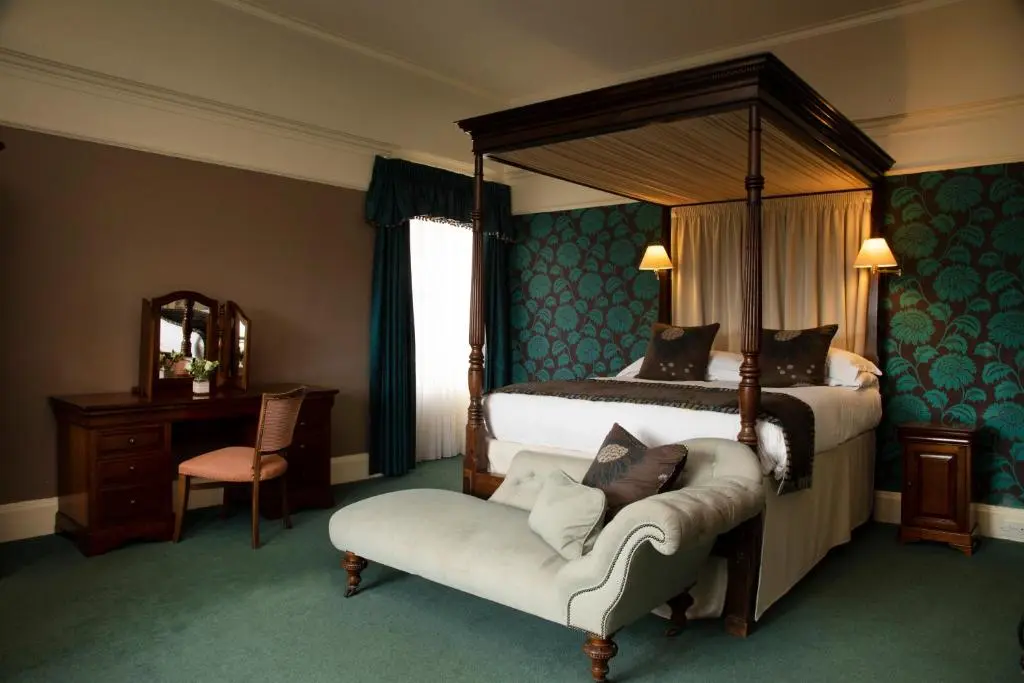 a bedroom with a canopy bed and a chair at Loch Ness Country House Hotel in Inverness