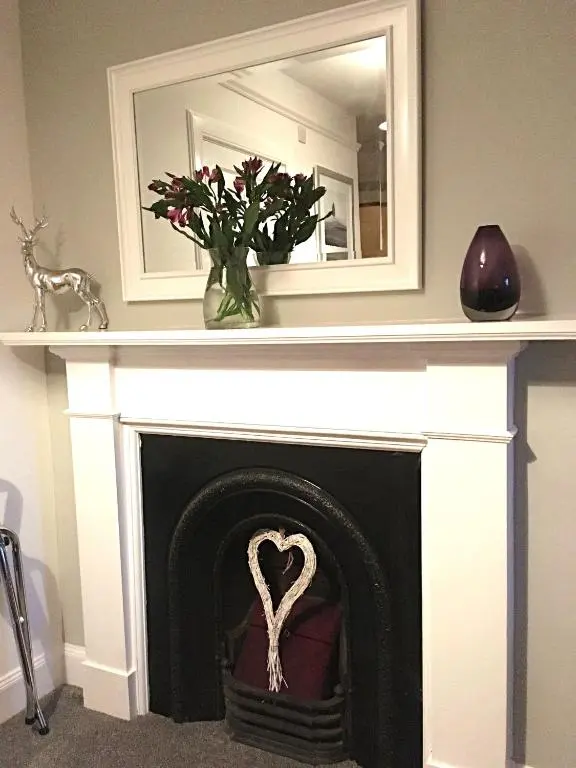 a fireplace with a mirror above it and a vase with flowers at Urrard B&B in Dingwall