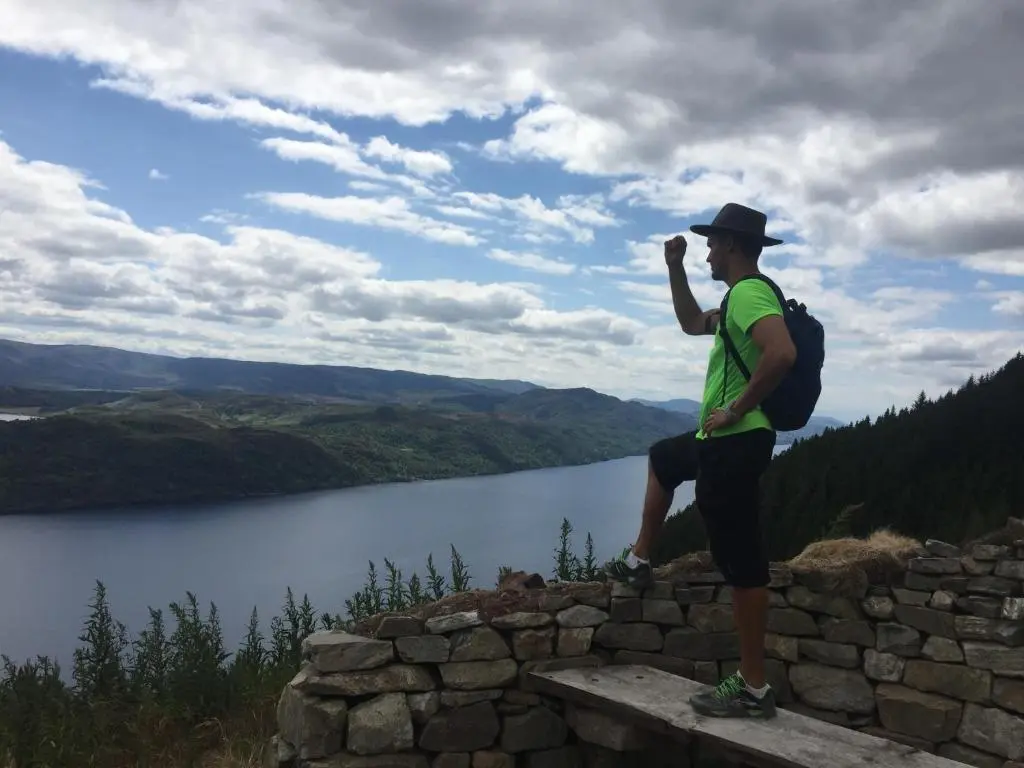 a man with a backpack standing on a wall overlooking a lake at Loch Ness Lochside Hostel - Over 16s Only in Invermoriston