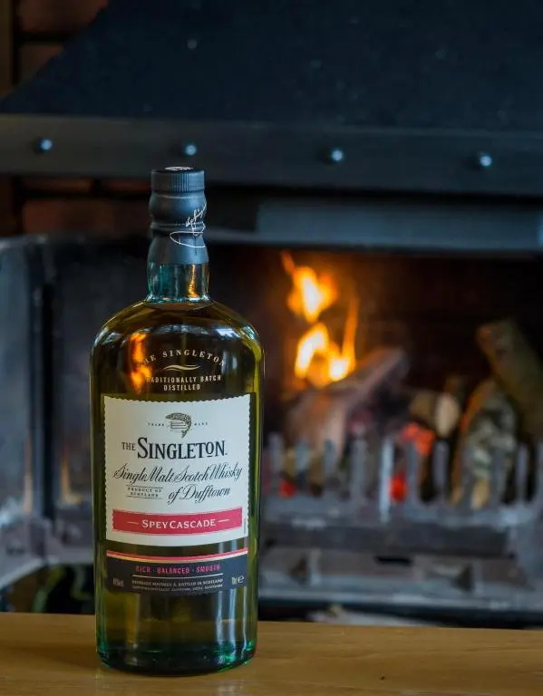 a bottle of whiskey sitting on a table in front of a fireplace at Loch Ness Lochside Hostel - Over 16s Only in Invermoriston