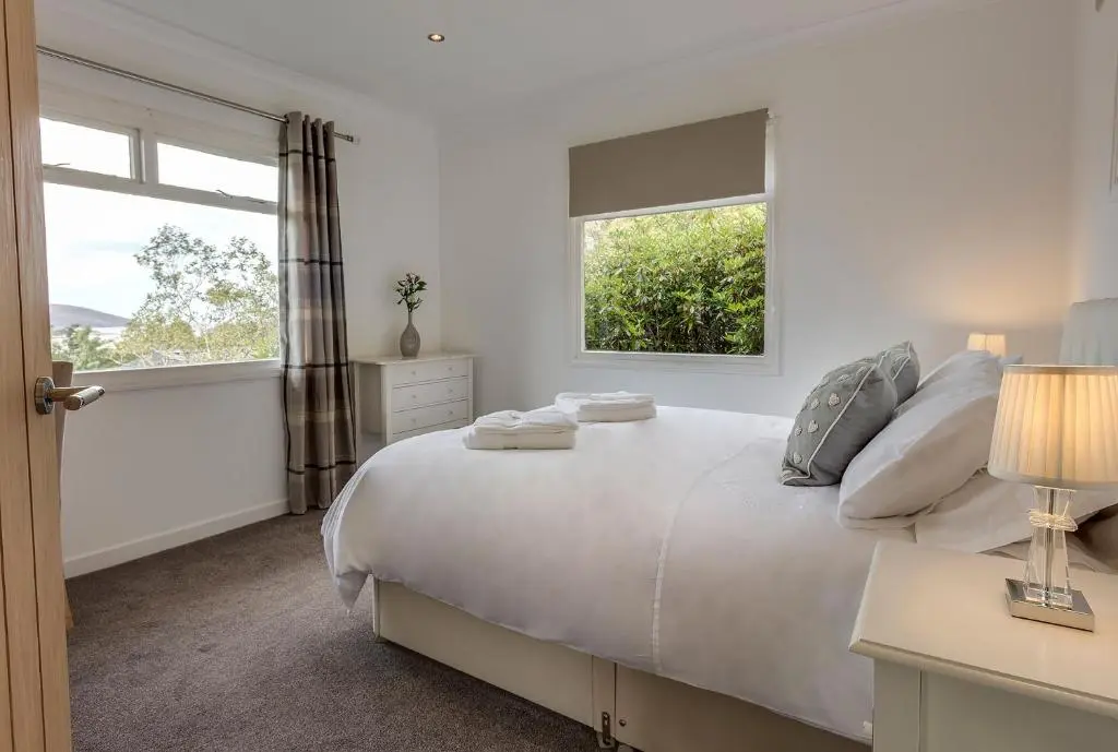a white bedroom with a large bed with two windows at Loch Broom Cabins Seaviews& Petfriendly in Leckmelm