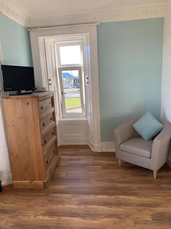 a living room with a tv and a chair and a dresser at The Ship Inn in Invergordon