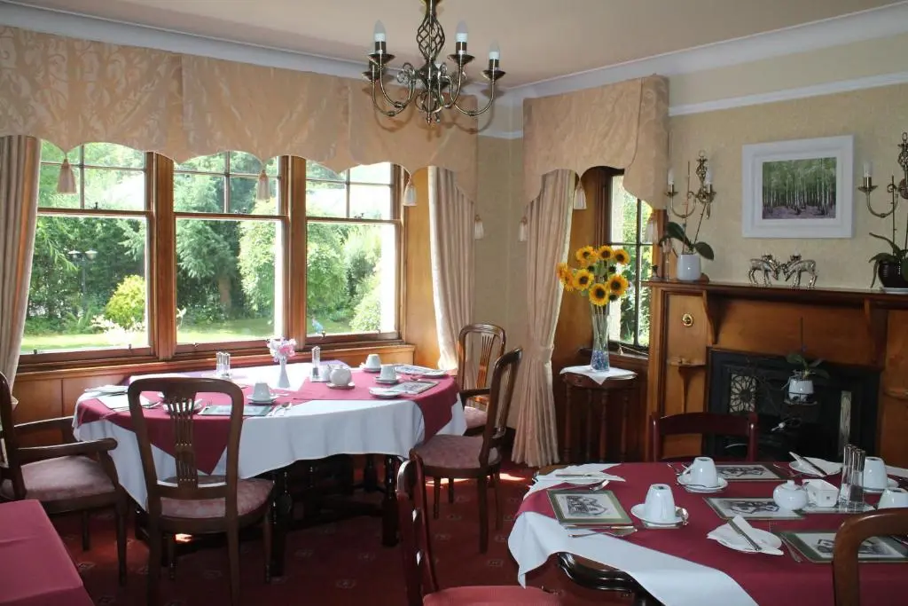 a dining room with tables and chairs and windows at Dalgreine Guest House in Blair Atholl