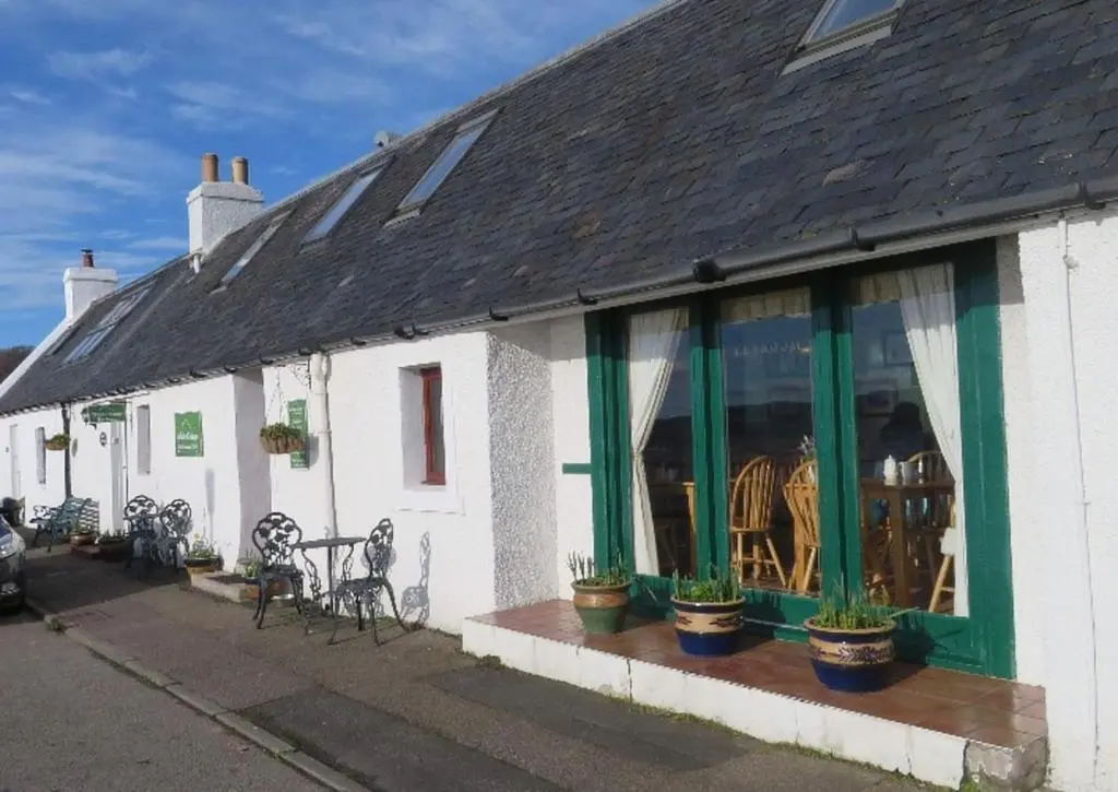 a white building with green windows and plants at White Cottage B&B in North Kessock