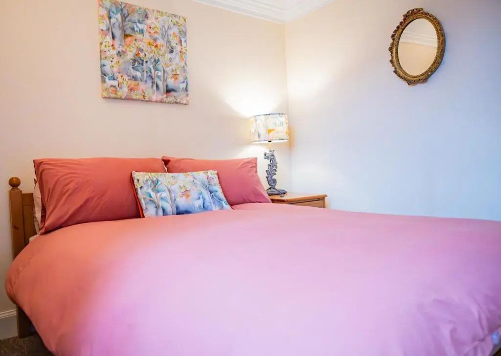 a bedroom with a pink bed and a mirror at East Wing Apartment in Elgin in Elgin
