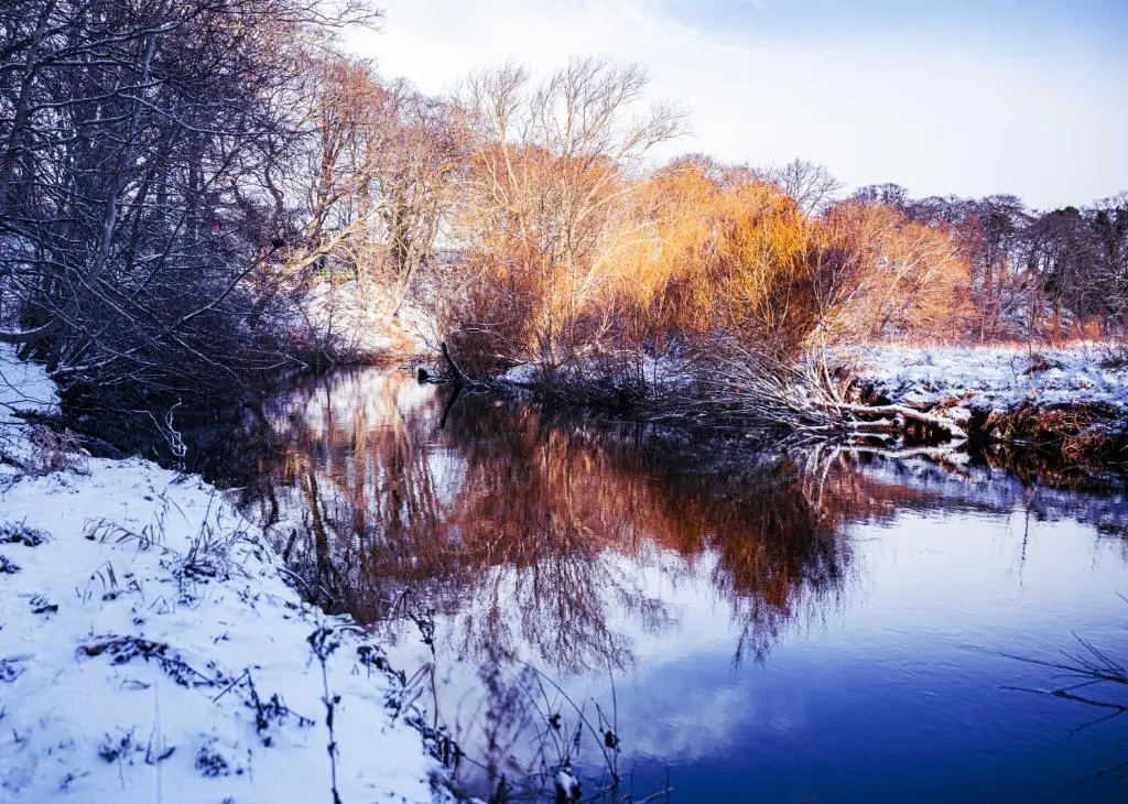a river with snow on the water and trees at East Wing Apartment in Elgin in Elgin