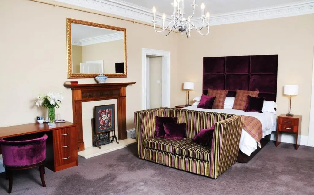 a bedroom with a bed and a chair and a mirror at Tor-Na-Coille Hotel in Banchory