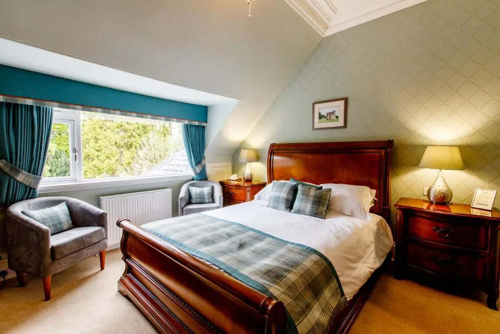 a bedroom with a bed and a chair and a window at Tor-Na-Coille Hotel in Banchory