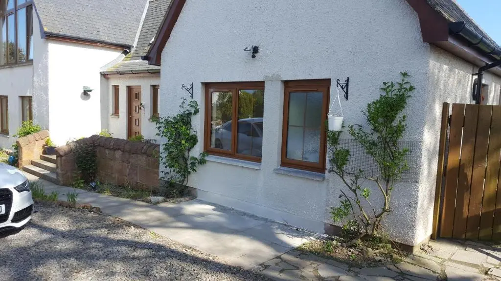 a white house with a window and a fence at Canterra Cottage in Tain