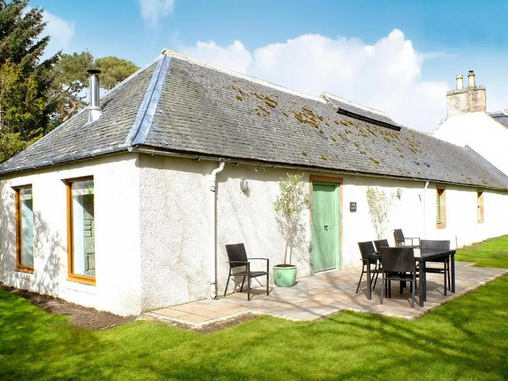 a white cottage with a table and chairs outside at The Barn in Ankerville