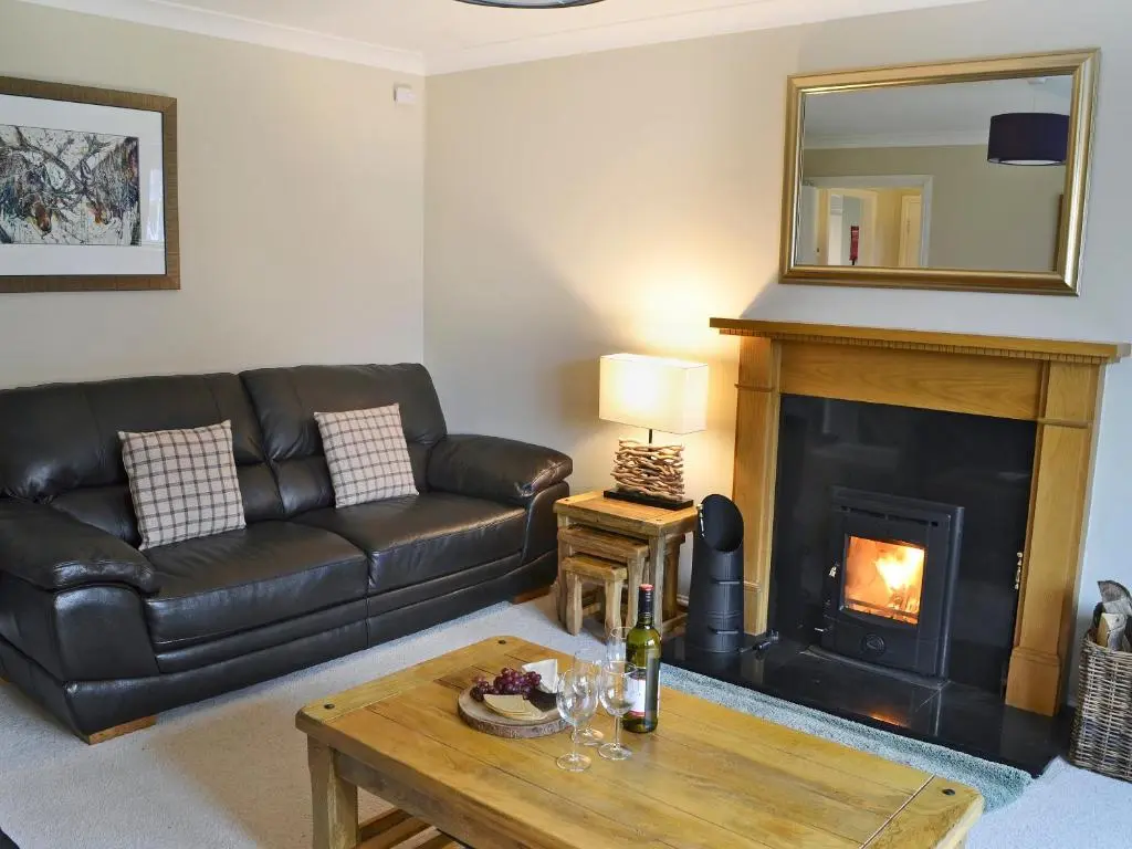 a living room with a leather couch and a fireplace at Stags Neuk in Aviemore