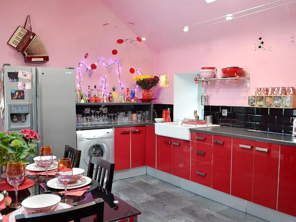 a kitchen with red cabinets and a pink wall at Sea Yonder in Buckie