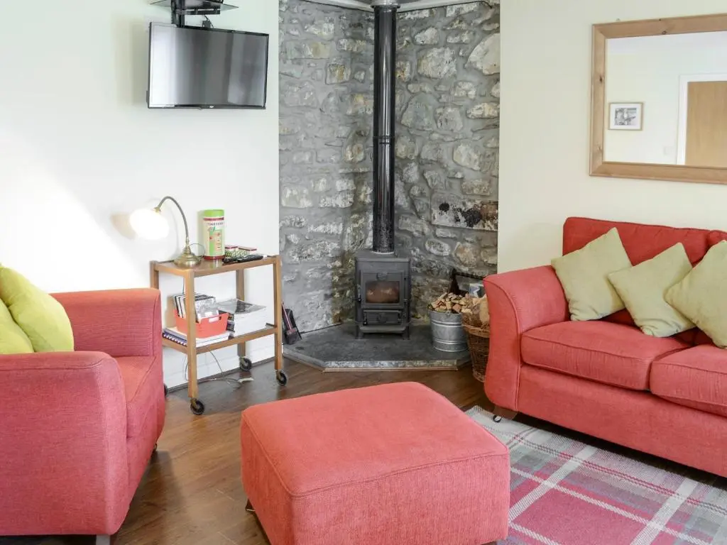 a living room with two red chairs and a fireplace at Birch Cottage in Glenrossal