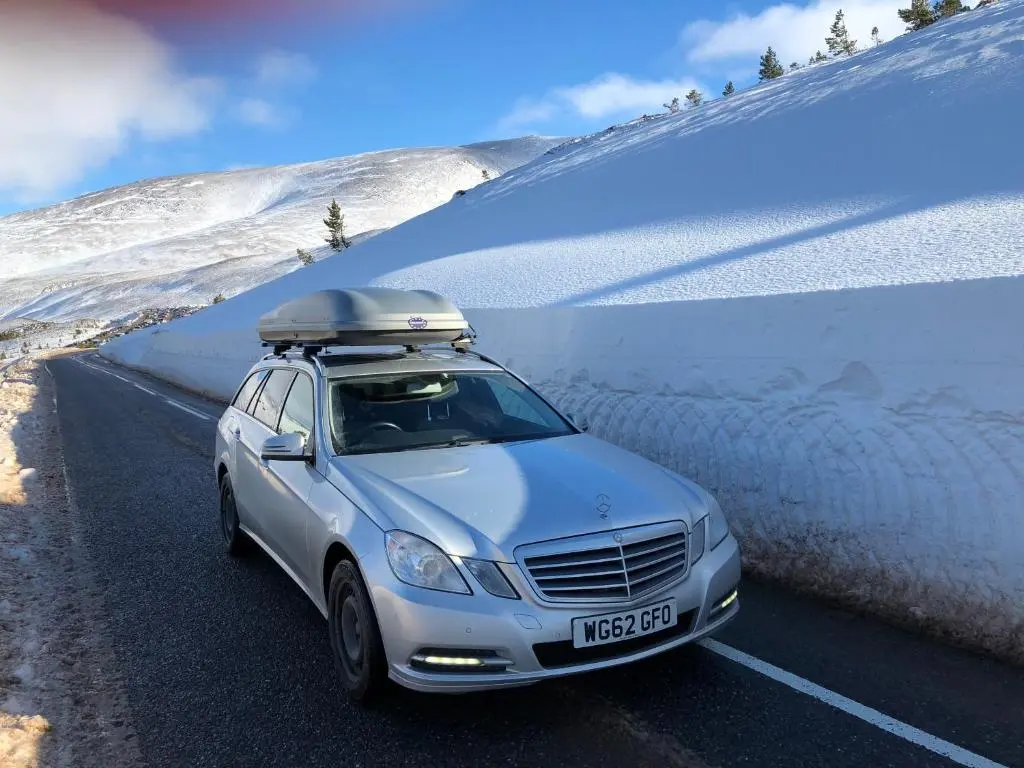 a car with a surfboard on the roof driving down a snow covered road at Ventoux in Aviemore