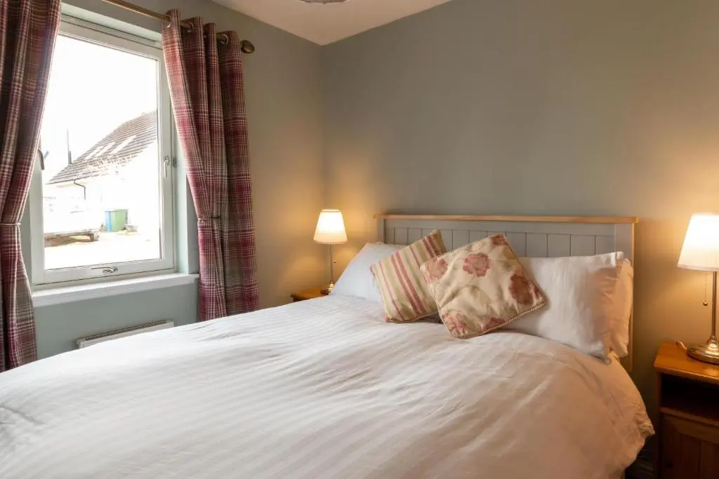 a bedroom with a white bed with two pillows and a window at Tigh na Lochan in Aviemore