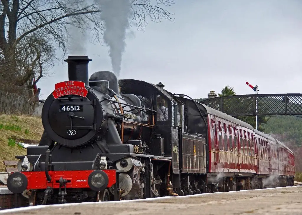 a steam engine train is coming down the tracks at Tigh na Lochan in Aviemore