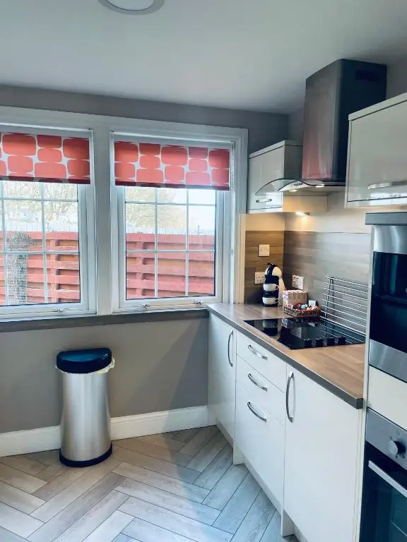 a kitchen with white cabinets and two windows at Apartment 101 Kingsmills Road in Inverness