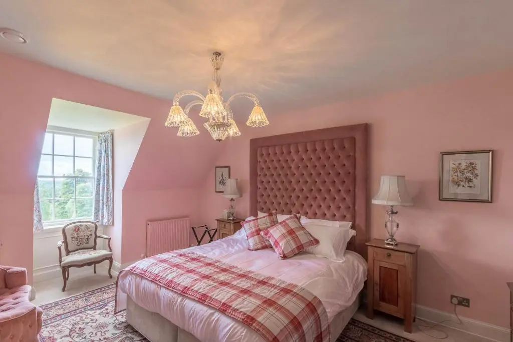 a pink bedroom with a bed and a chandelier at Blervie House in Forres
