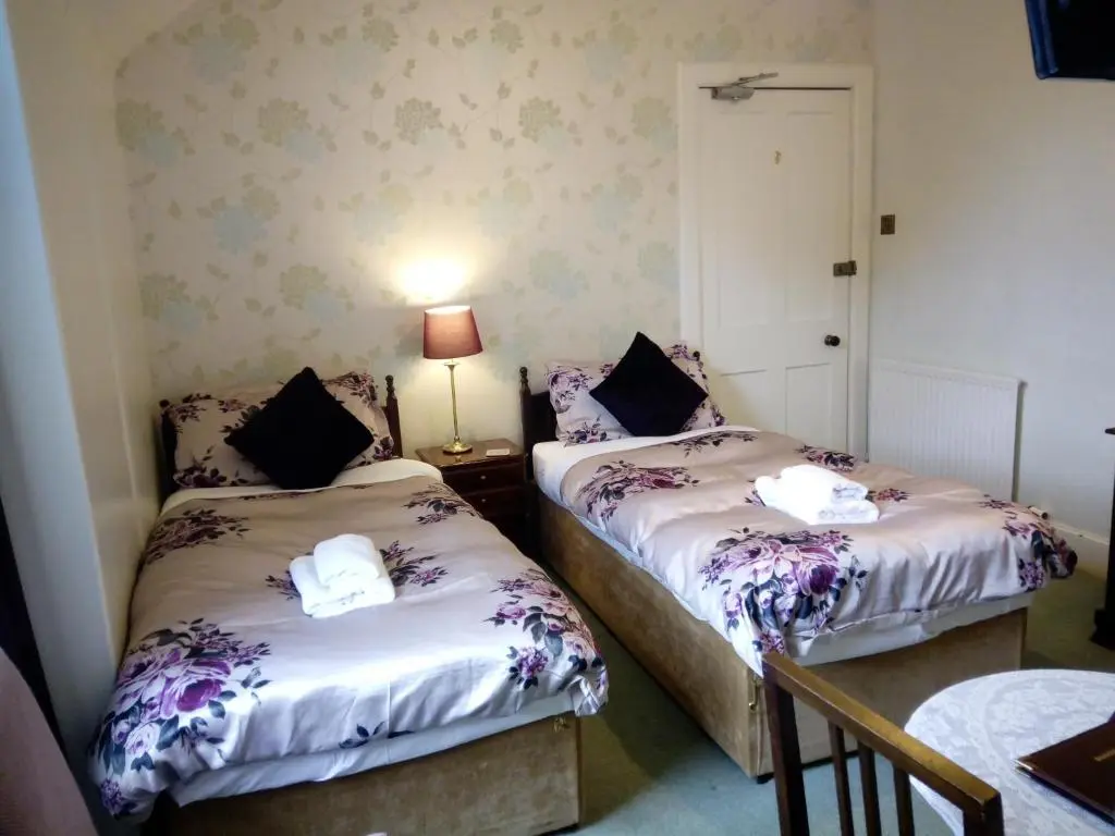 two twin beds in a room with a lamp on a table at Dunallan Guest House in Grantown on Spey