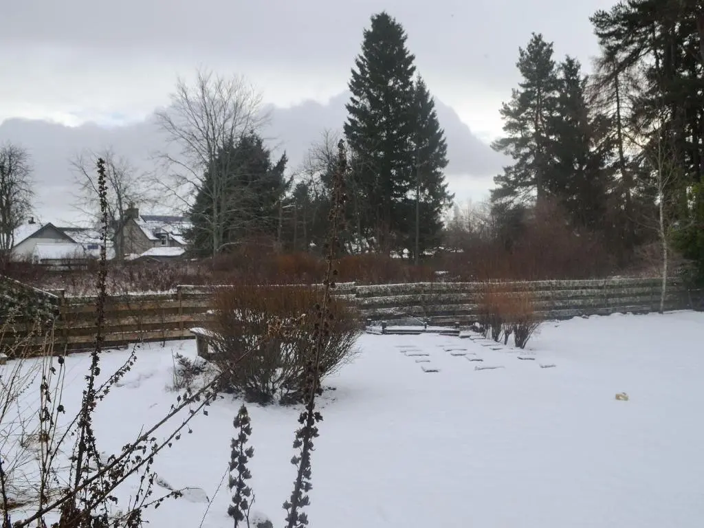 a pond covered in snow next to a fence at West End Cottage in Carrbridge