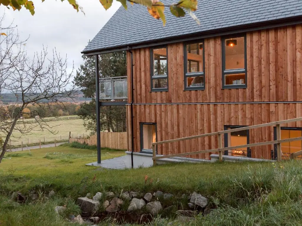 a wooden house with a deck and windows at Strathspey Lodge in Duthil