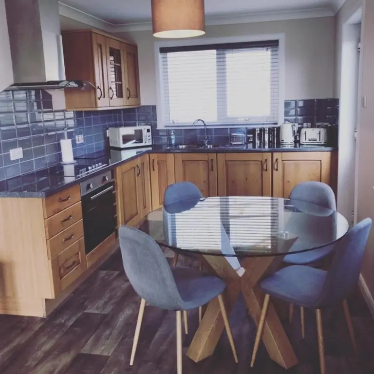a kitchen with a glass table and blue chairs at Malva - Modern 2 Bedroom Bungalow in Wick Sleeps 4 with private parking - NC500 Route in Wick