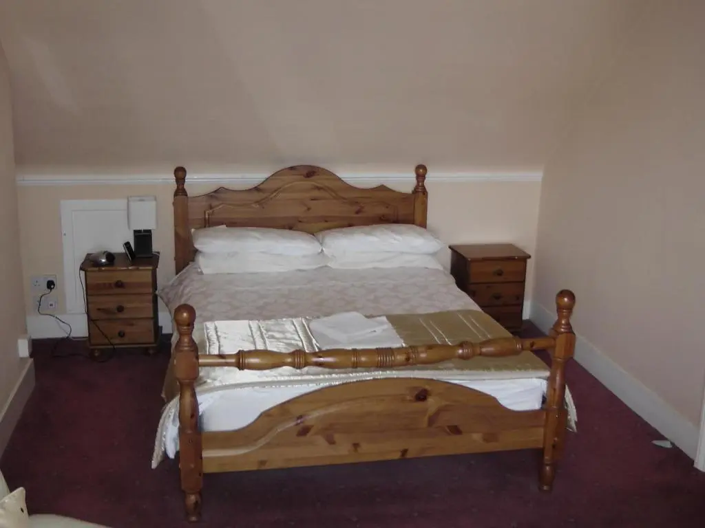 a bedroom with a wooden bed and two night stands at Beeches Guest House in Dyce