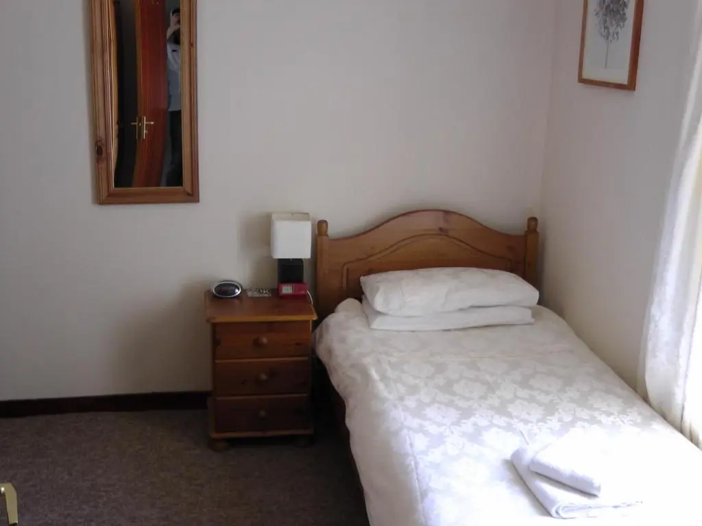 a bedroom with a bed and a dresser with a mirror at Beeches Guest House in Dyce