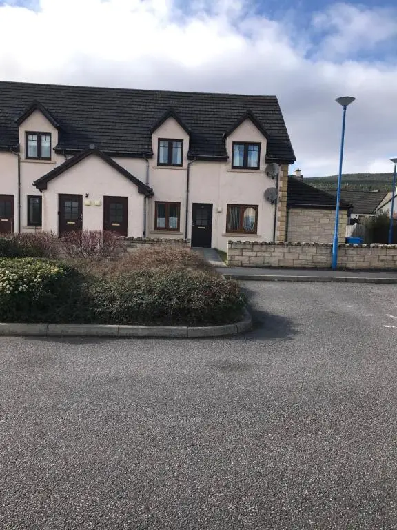 a white house with a black roof on a street at Christiesholidayhomes in Aviemore