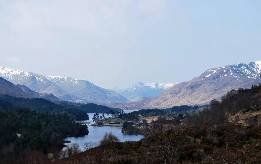 a lake in the middle of a valley with snow covered mountains at Doric House in Inverness