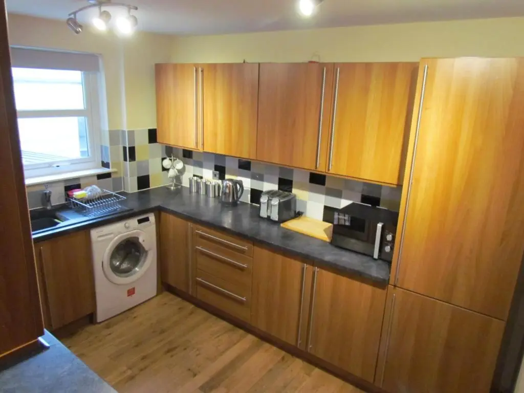 a kitchen with wooden cabinets and a washing machine at Farraline Court in Inverness