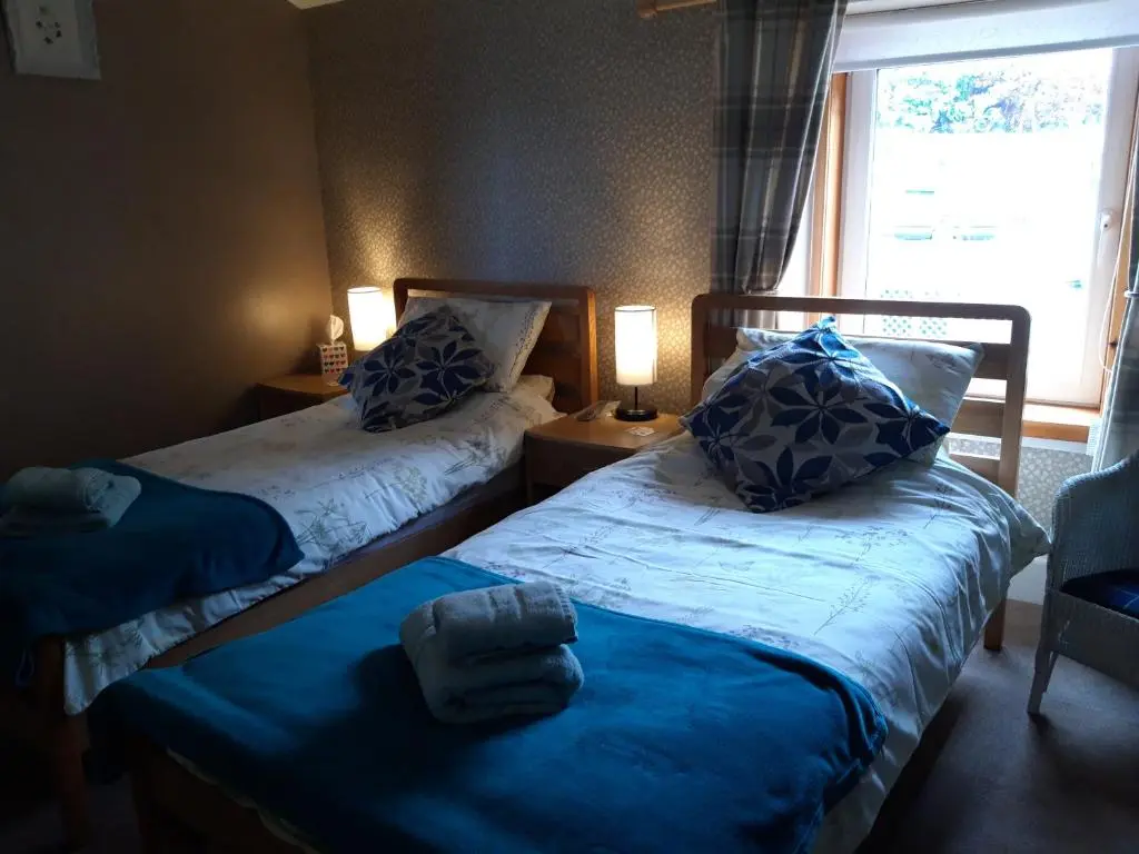 a bedroom with two beds with blue pillows and a window at Gowanbrae in Dufftown