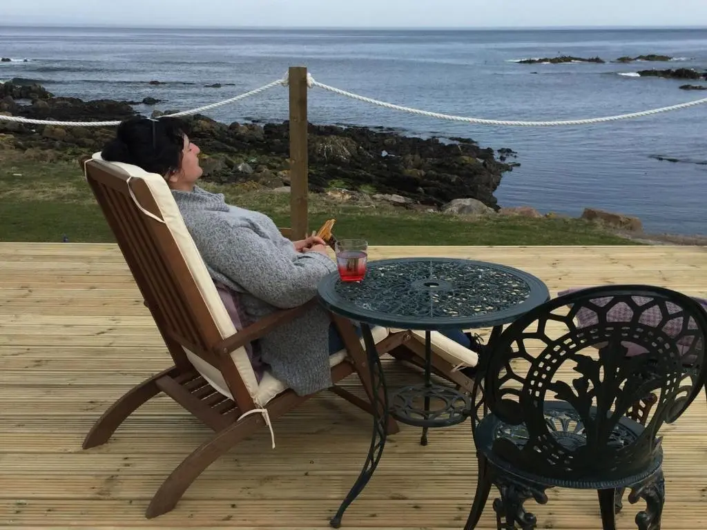 a woman sitting in a chair at a table at Pew with a View - Seafront Cottages in Sandhaven