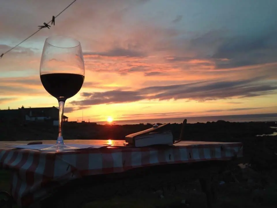 a glass of wine sitting on a table with the sunset at Pew with a View - Seafront Cottages in Sandhaven