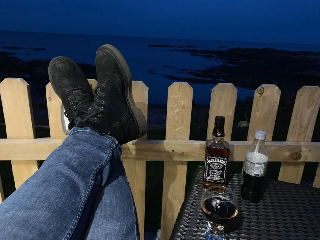 a person with their feet on a fence with two bottles of beer at Door to the Shore - Seafront Cottages in Sandhaven