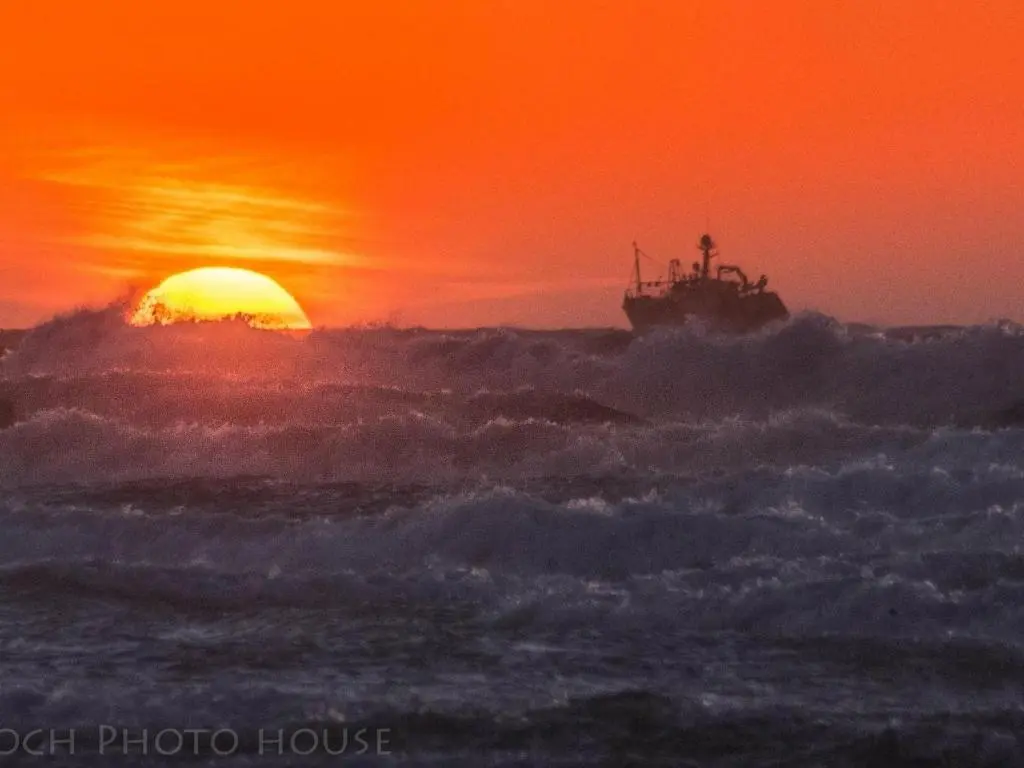 a boat in the ocean with the sunset in the background at Door to the Shore - Seafront Cottages in Sandhaven