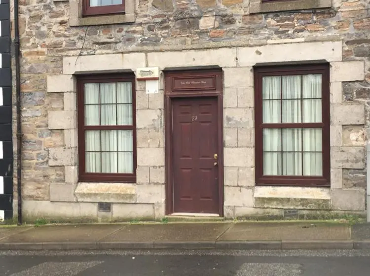 a brick building with a brown door and two windows at The Old Chemist in Cullen