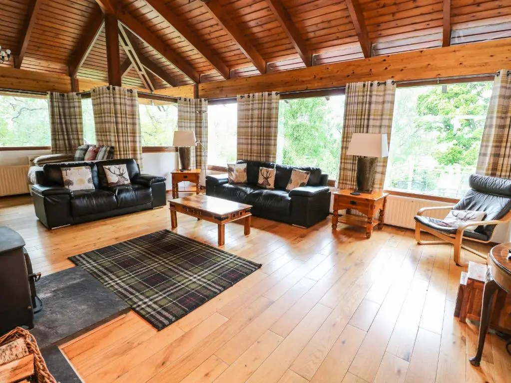 a living room with black leather furniture and large windows at Katchana in Insh
