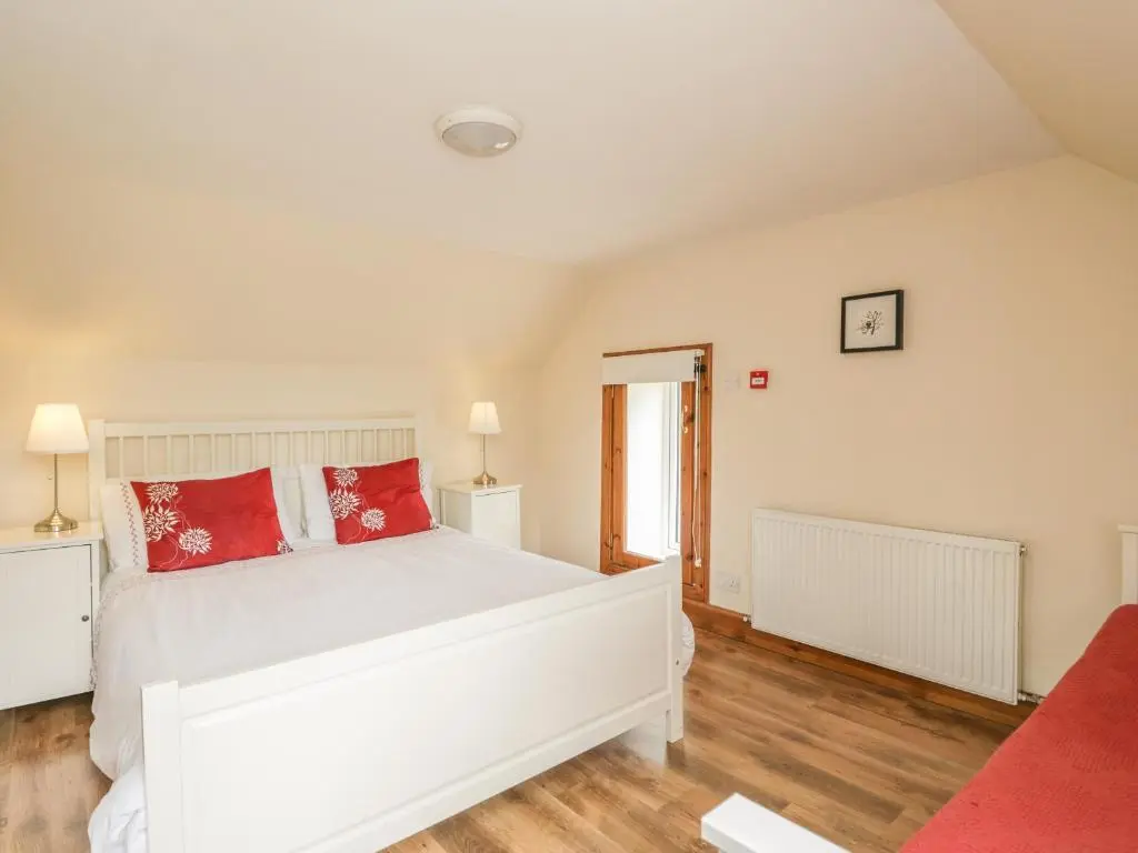a bedroom with a white bed with red pillows at 10 Monarch Country Apartments in Newtonmore