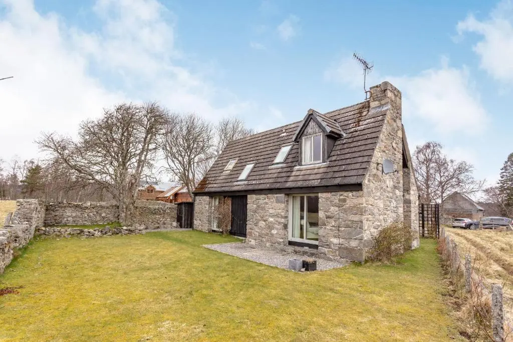 a stone house with a gambrel roof on a field at Inshcraig in Kincraig