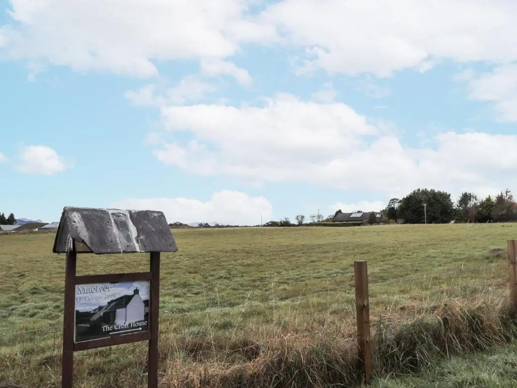 a sign in a field next to a fence at The Croft House in Muir of Ord