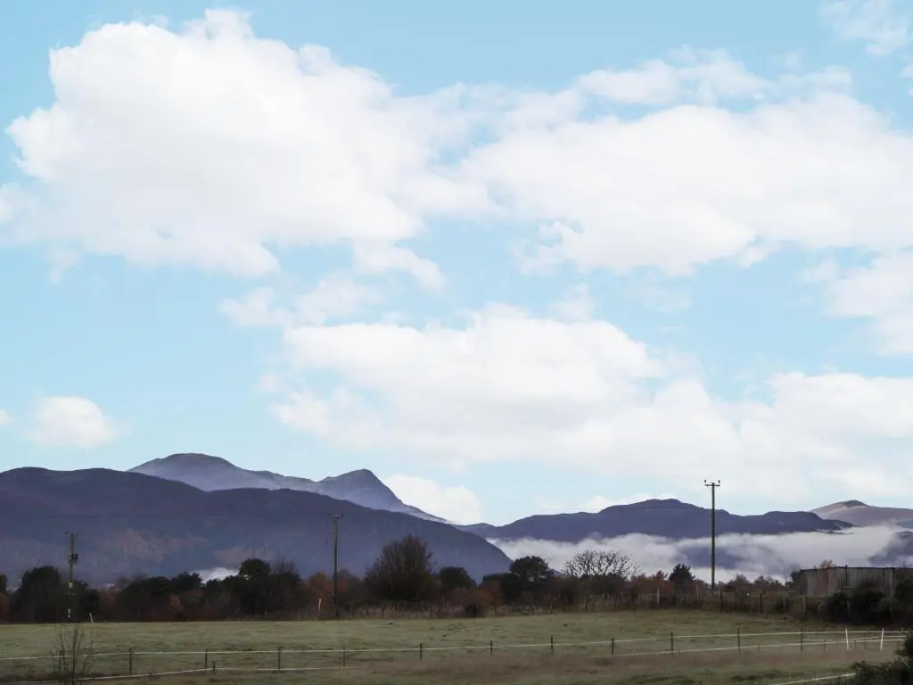 a field with a fence and mountains in the background at The Croft House in Muir of Ord