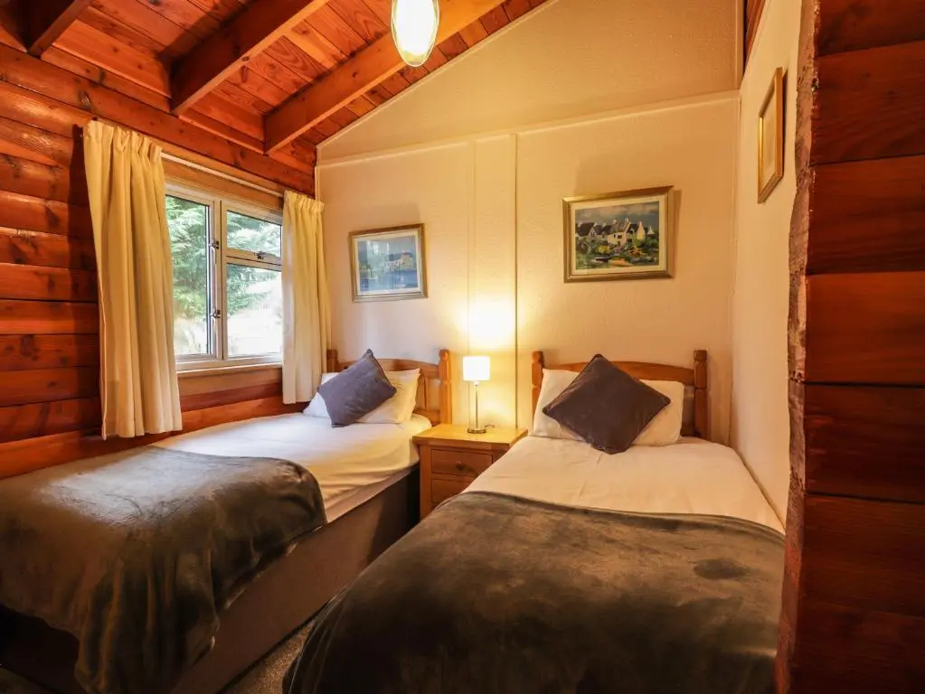 two beds in a room with a window at Spruce Lodge in Strathpeffer