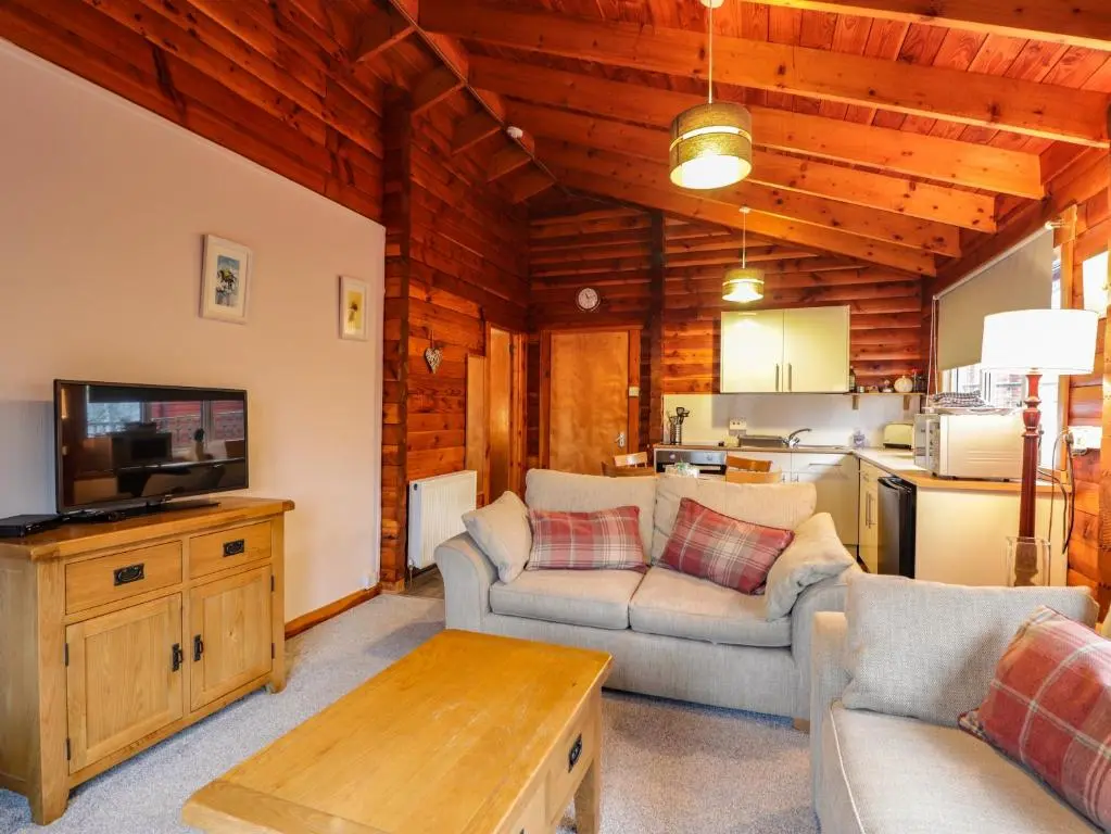 a living room with a couch and a tv and a table at Spruce Lodge in Strathpeffer