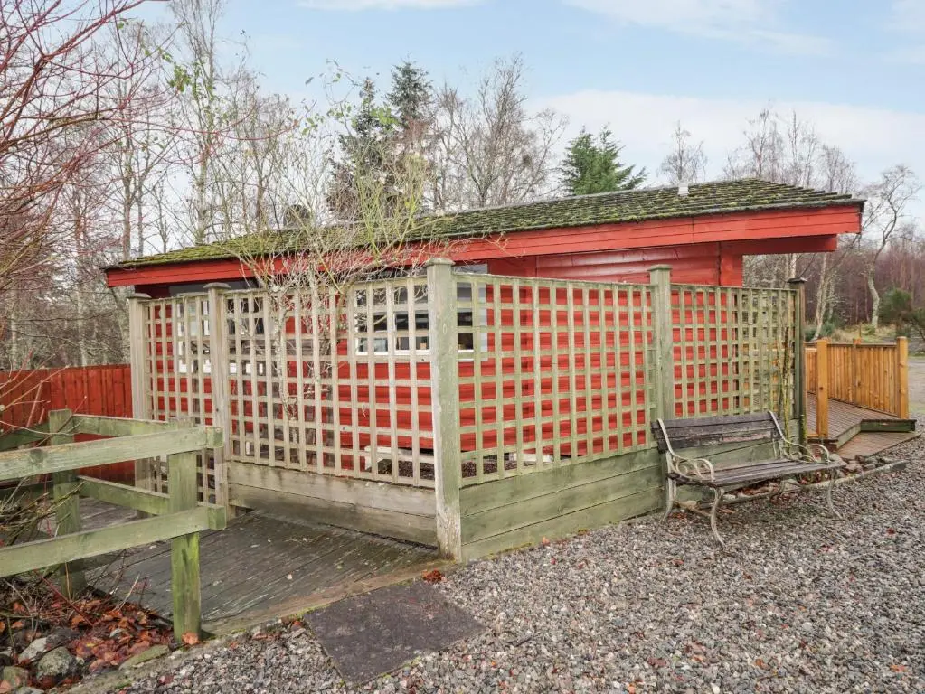 a red building with a gate and a bench at Spruce Lodge in Strathpeffer