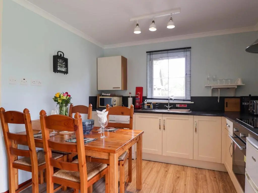 a kitchen with a wooden table with chairs and a dining room at Pebbles Cottage in Contin